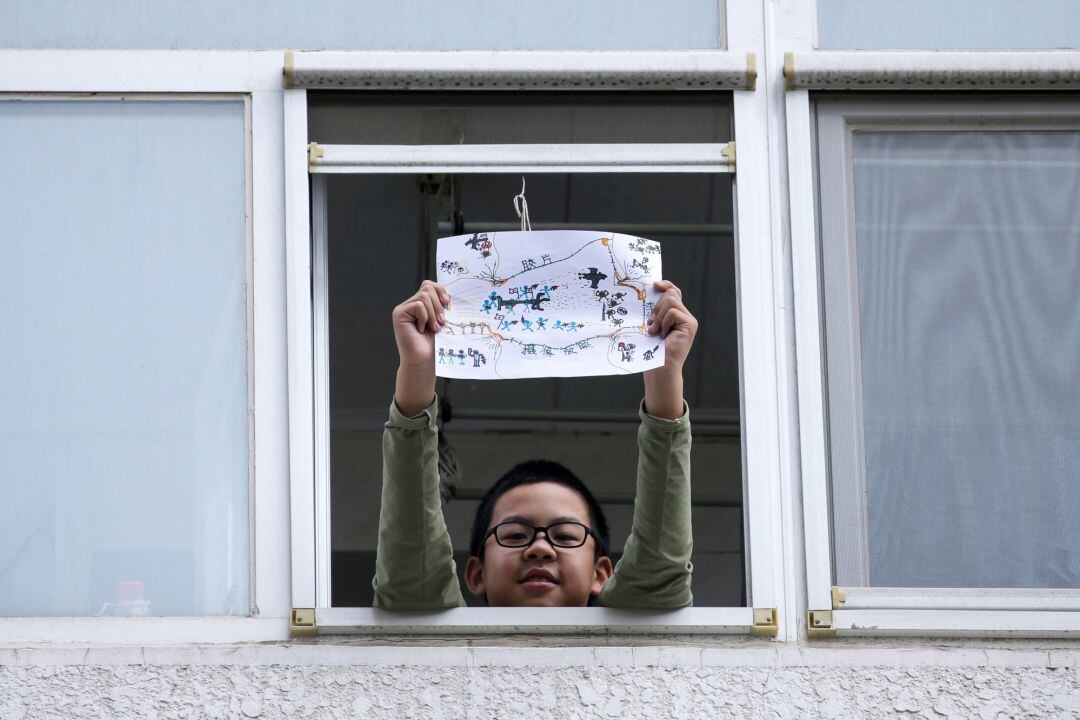 Un niño muestra un dibujo con cómo ve la crisis del Coronavirus desde la ventana de su casa en Pekín, China