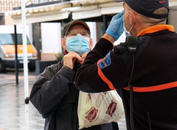 Un hombre recibe las indicaciones de cómo colocarse la mascarilla por parte de un agente local