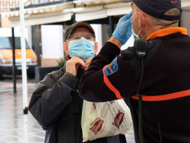 Un hombre recibe las indicaciones de cómo colocarse la mascarilla por parte de un agente local
