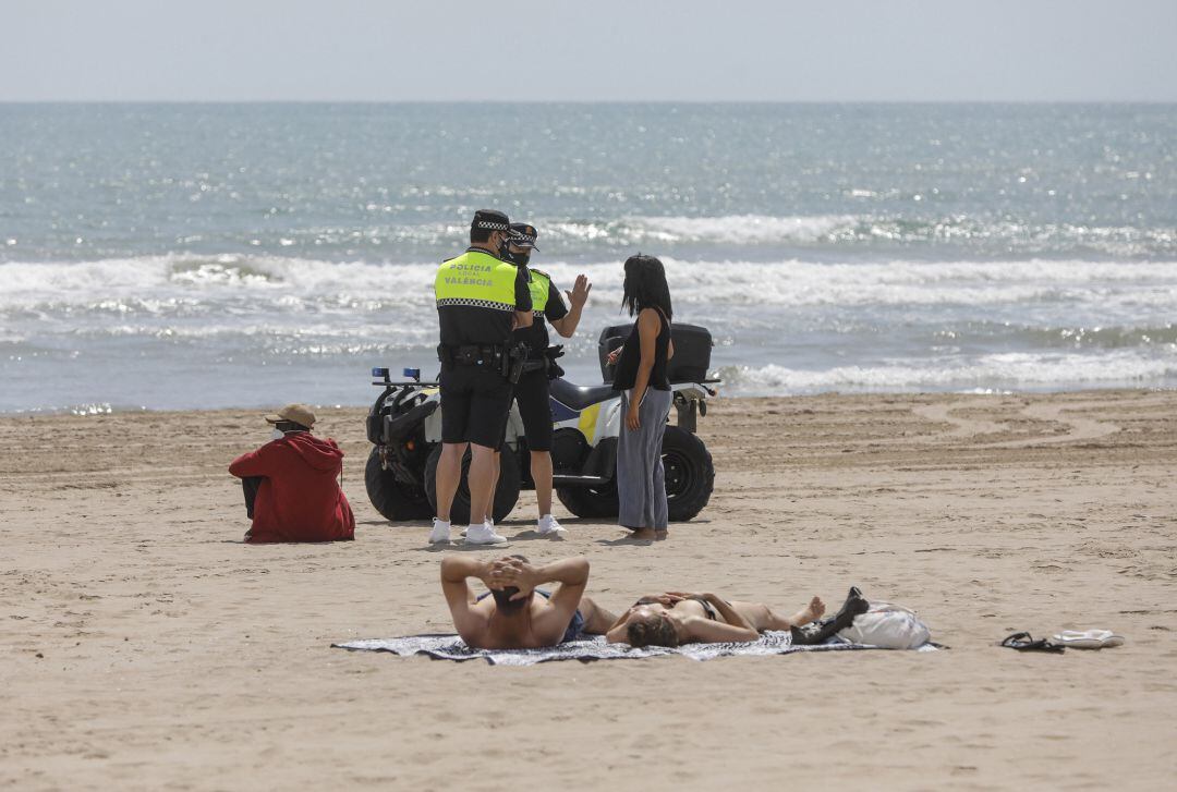 Dos policías municipales hablan con una mujer en una playa de València