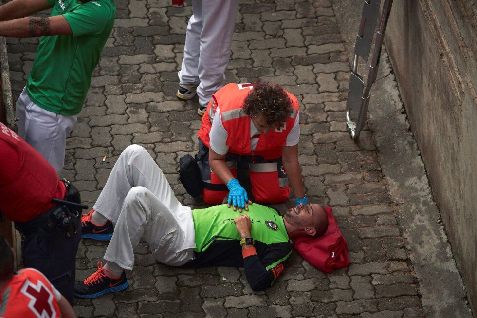 Un miembro de los servicios sanitarios atiende a un mozo que ha sufrido un percance durante el tercer encierro de los Sanfermines 2019.