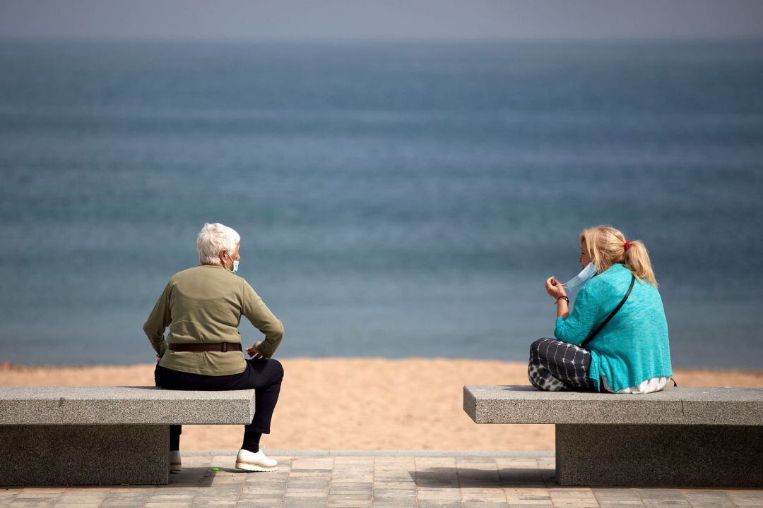 Dos mujeres hablan en unos bancos de la playa de L'Escala (Girona) este jueves mientras Girona se mantiene en la fase 1 de la desescalada.