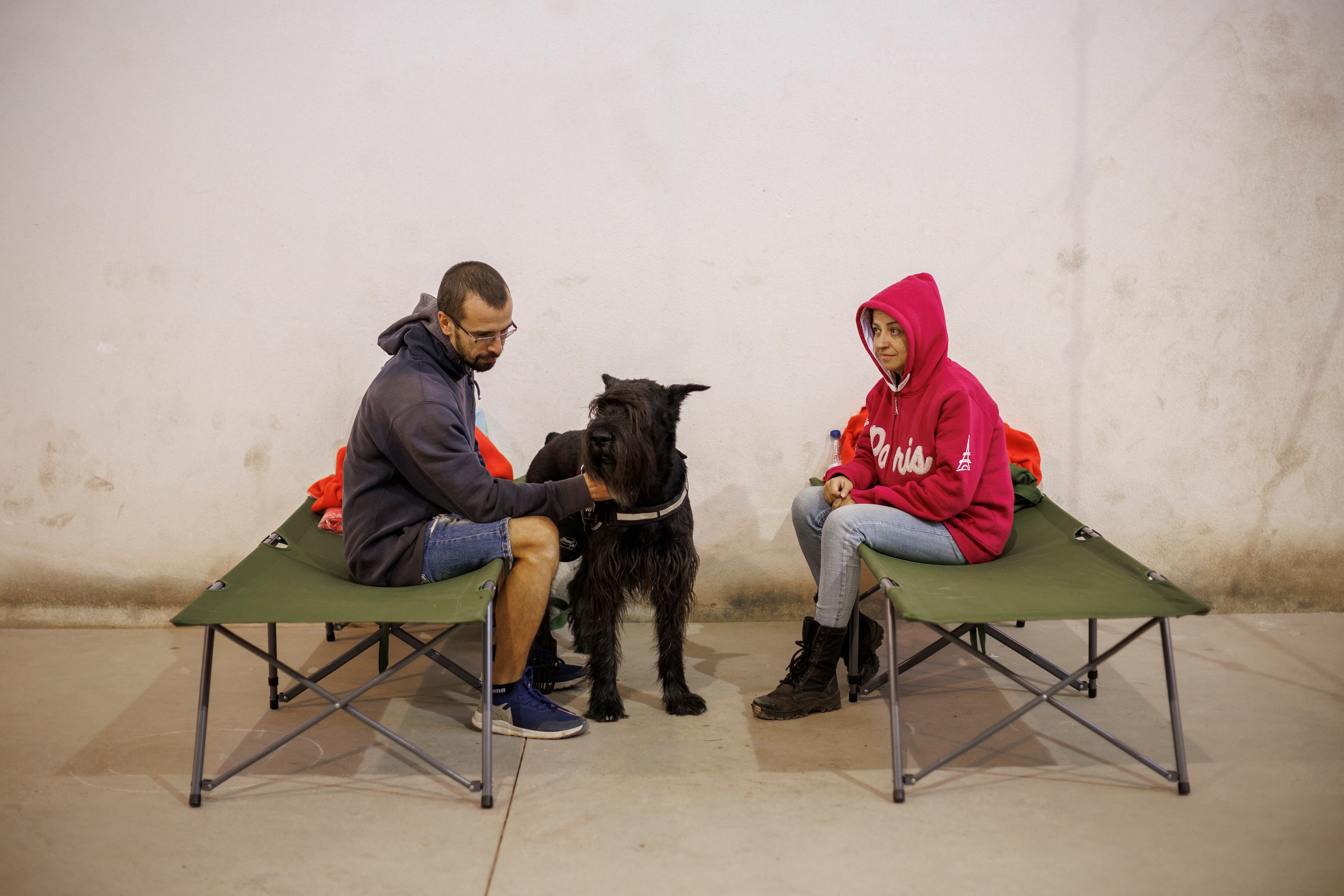 GRAFCVA77560. BEJÍS (CASTELLÓN), 18/08/2022.-.-La lluvia caída durante esta madrugada en el entorno del incendio forestal de Bejís, en la comarca castellonense del Alto Palancia, ha reducido la llama hasta casi desaparecer en todo el perímetro.Según han informado este jueves fuentes de Emergencias de la Generalitat, se han registrado en esta zona mediciones de entre 14 y 20 litros por metro cuadrado, que unido a una mayor humedad relativa en el ambiente han sido factores positivos, aunque todavía quedan zonas muy calientes.En la imagen, un matrimonio ruso evacuado del pueblo de Sacañet espera en el albergue que la Cruz Roja ha instalado en el polideportivo de Alcublas a la espera de poder regresar a sus casas. EFE/Biel Aliño