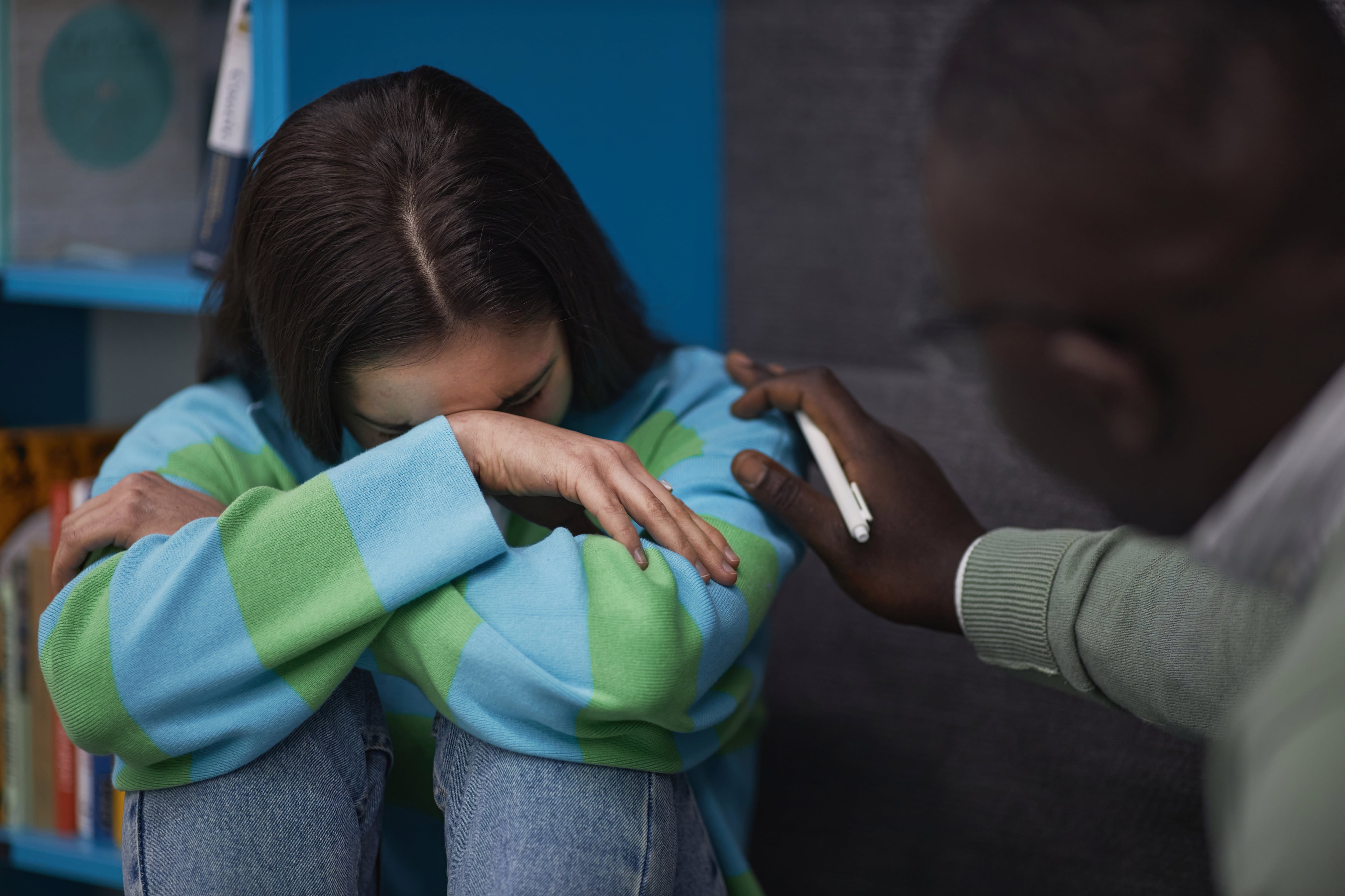 Close up of teenage girl crying in therapy session with psychologist supporting