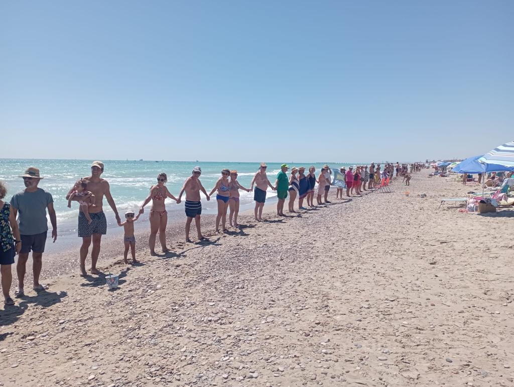 Vecinos y vecinas de las playas del norte de Sagunt juntan sus manos en la orilla del mar.