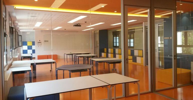 Imatge d'una de les aules del centres amb taules i cadires agrupades, més llum i grades al fons a la dreta