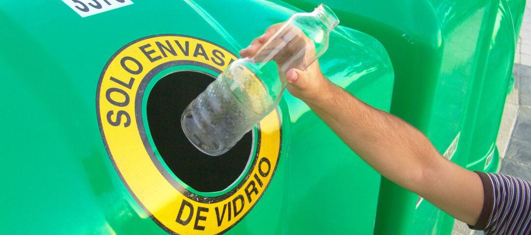 Una persona introduce una botella de vidrio en un contenedor verde.