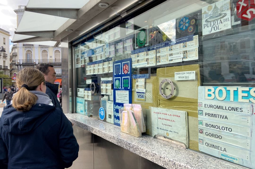 Dos personas compran décimos de Lotería de Navidad en una Administración en la plaza de Puerta del Sol, en Madrid (España).