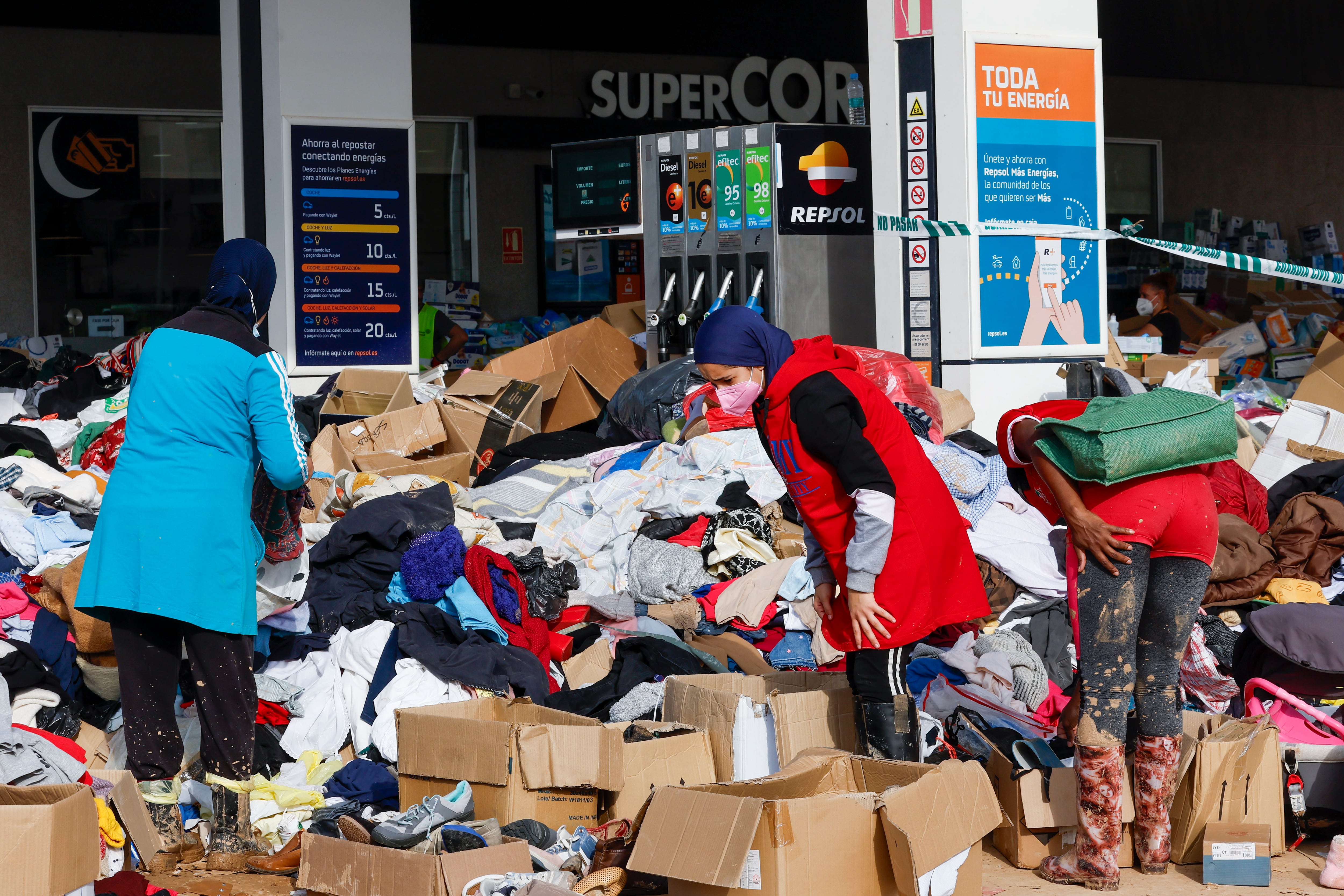 Varias personas rebuscan ente la ropa en una gasolinera reconvertida en punto de reparto de productos de primera necesidad, este martes, en la localidad valenciana de Catarroja.