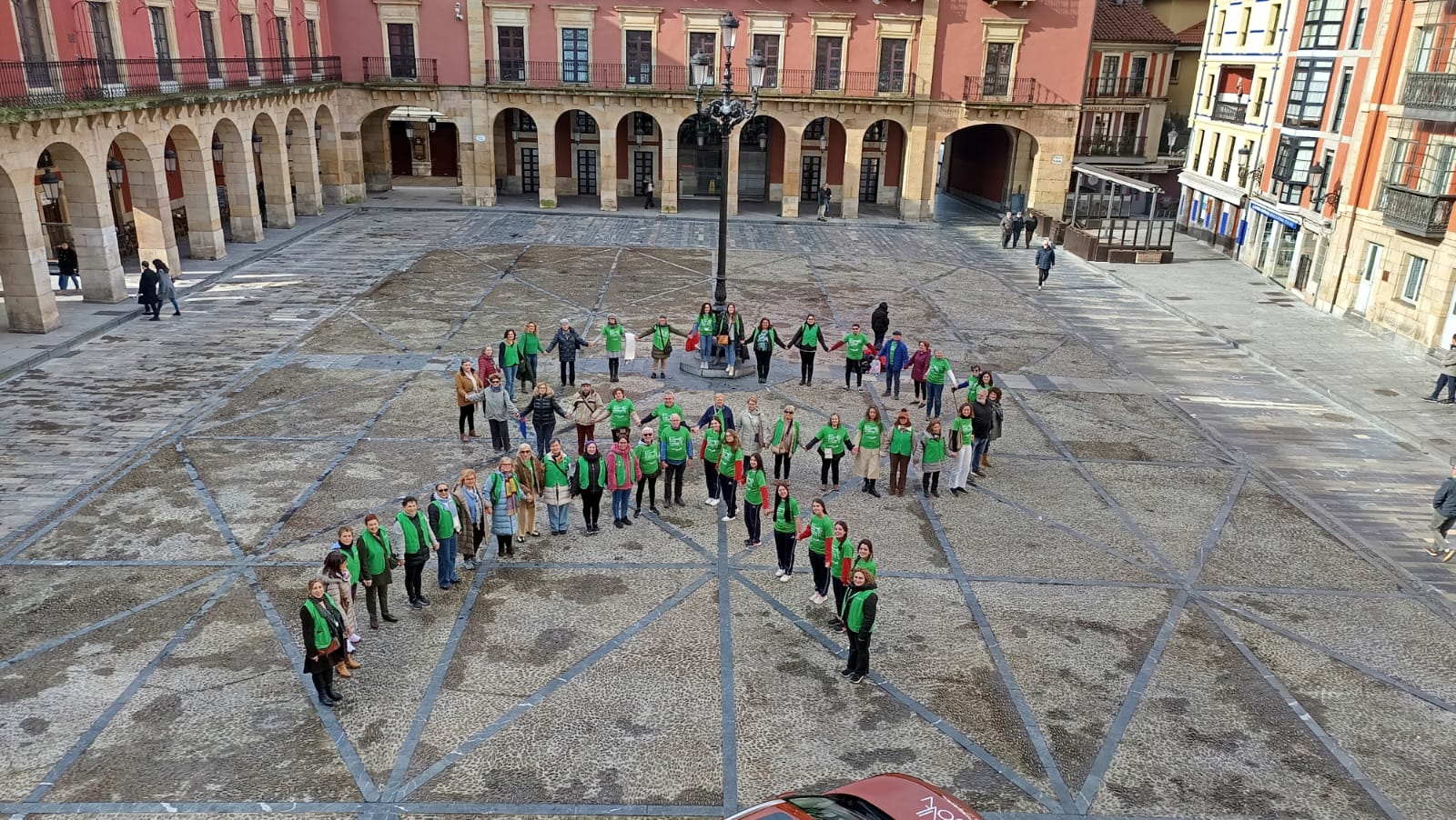 Miembros de la AECC forman un lazo en la plaza del Ayuntamiento de Gijón.