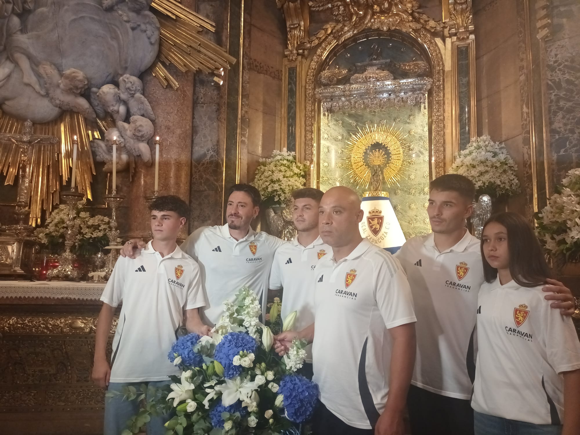 Cristian Álvarez, uno de los capitanes del primer equipo del Real Zaragoza junto a Guillermo Acín, del Deportivo Aragón; Hugo Pinilla, Juvenil A; Ana Forcén, Zaragoza Femenino; y José Luis Mansilla, Zaragoza Genuine, junto a las flores que ofrecen a la Virgen del Pilar en la ofrende tradicional de inicio de temporada