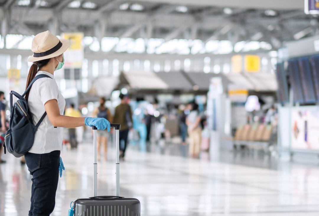 Turistas en aeropuerto con maleta y mascarilla.