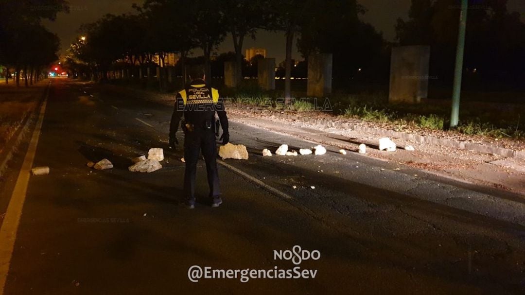 Policía local de Sevilla observa las piedras colocadas en la calzada, cerca del asentamiento chabolista de El Vacie 