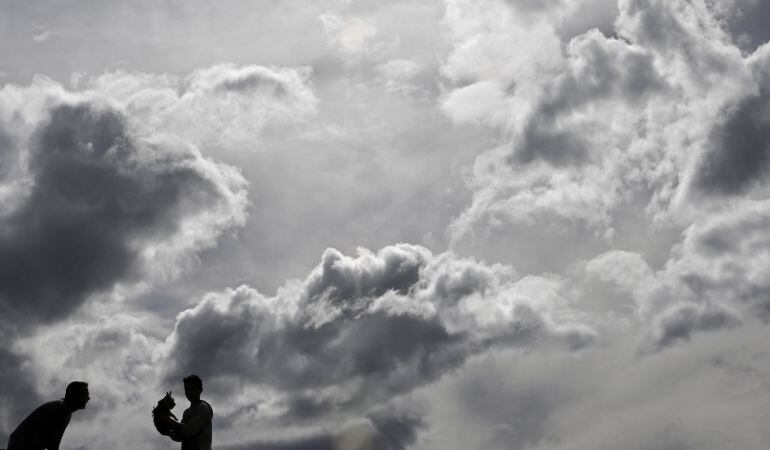 Dos personas juegan con su mascota bajo un manto de nubes en Pamplona.
