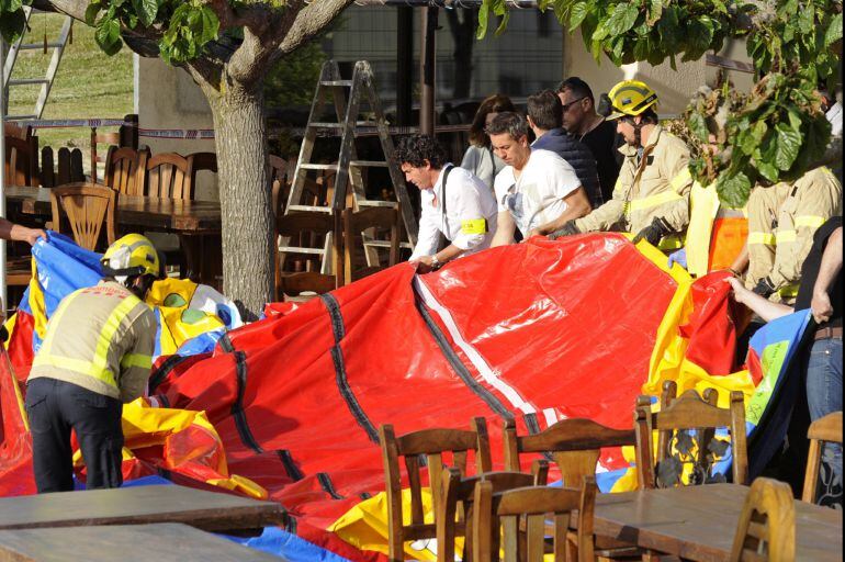 Varios operarios y bomberos retiran el castillo hinchable del restaurante Mas Oller, de Caldes de Malavella (Gerona), que ha volado unos 40 metros por encima del tejado del establecimiento