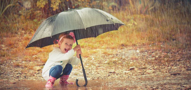 Una niña sonríe mientras se protege con un paraguas bajo la lluvia. 