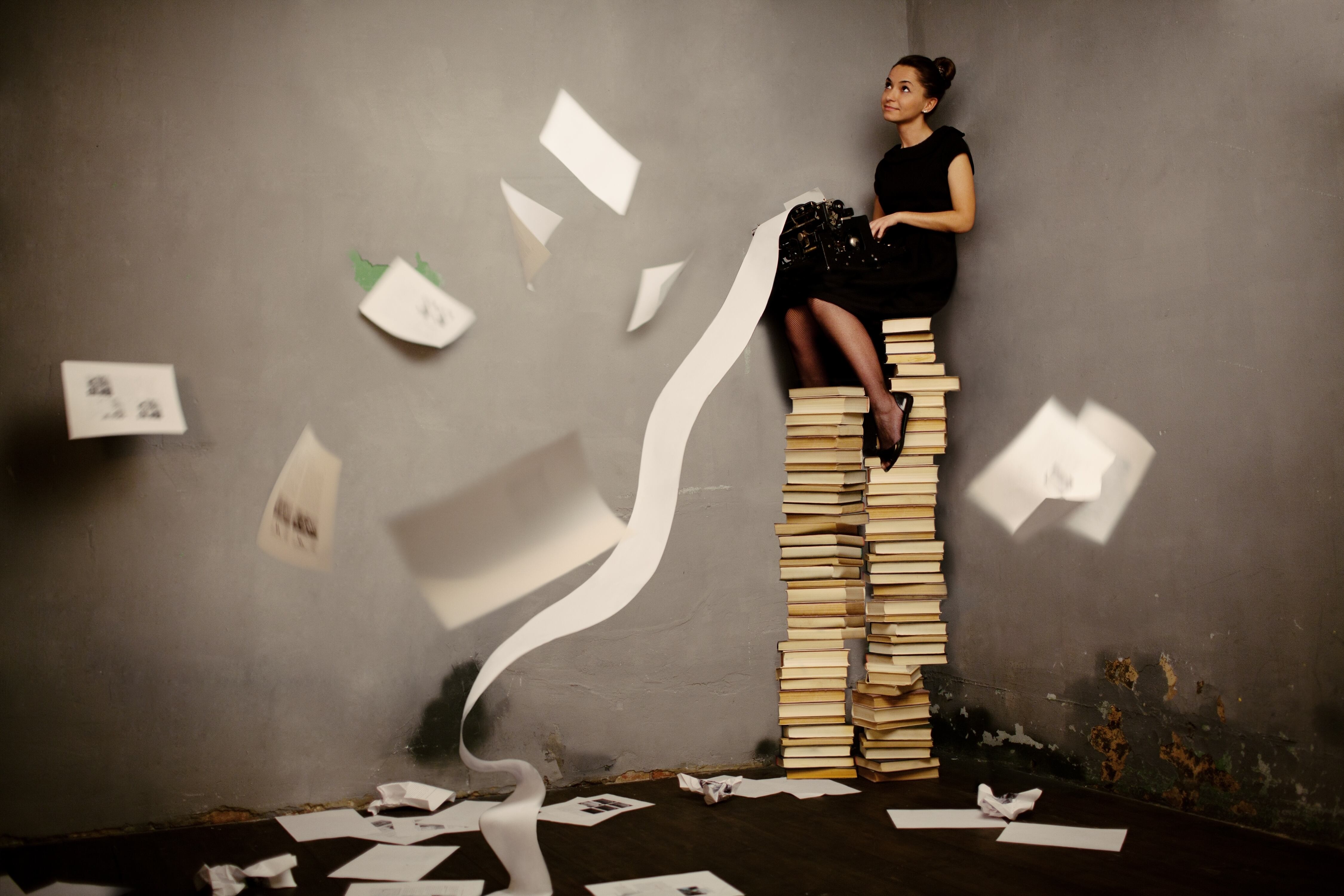 Mujer escribiendo sentada sobre una torre de libros.