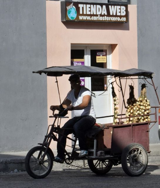 Un hombre pasa con su triciclo de ventas de productos, frente a un cartel con anuncio de compras on-line de una tienda cubana en La Habana