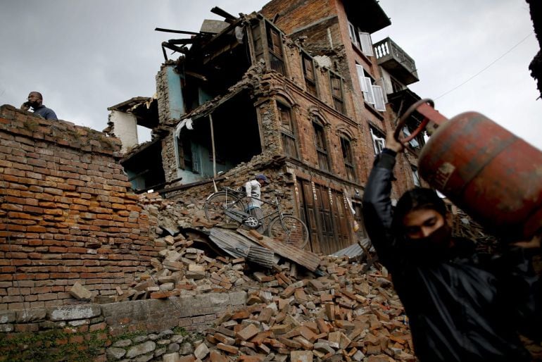 Un hombre sostiene una bombona y otro traslada una bicicleta encontrada entre los escombros de viviendas que quedaron destrozadas tras el terremoto del pasado sábado en Nepal