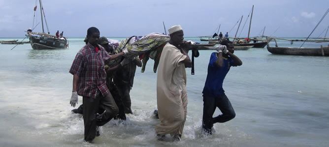 Algunas personas cargan con cuerpos de las víctimas de la embarcación que ha naufragado en Zanzíbar, en la playa de Nungwi