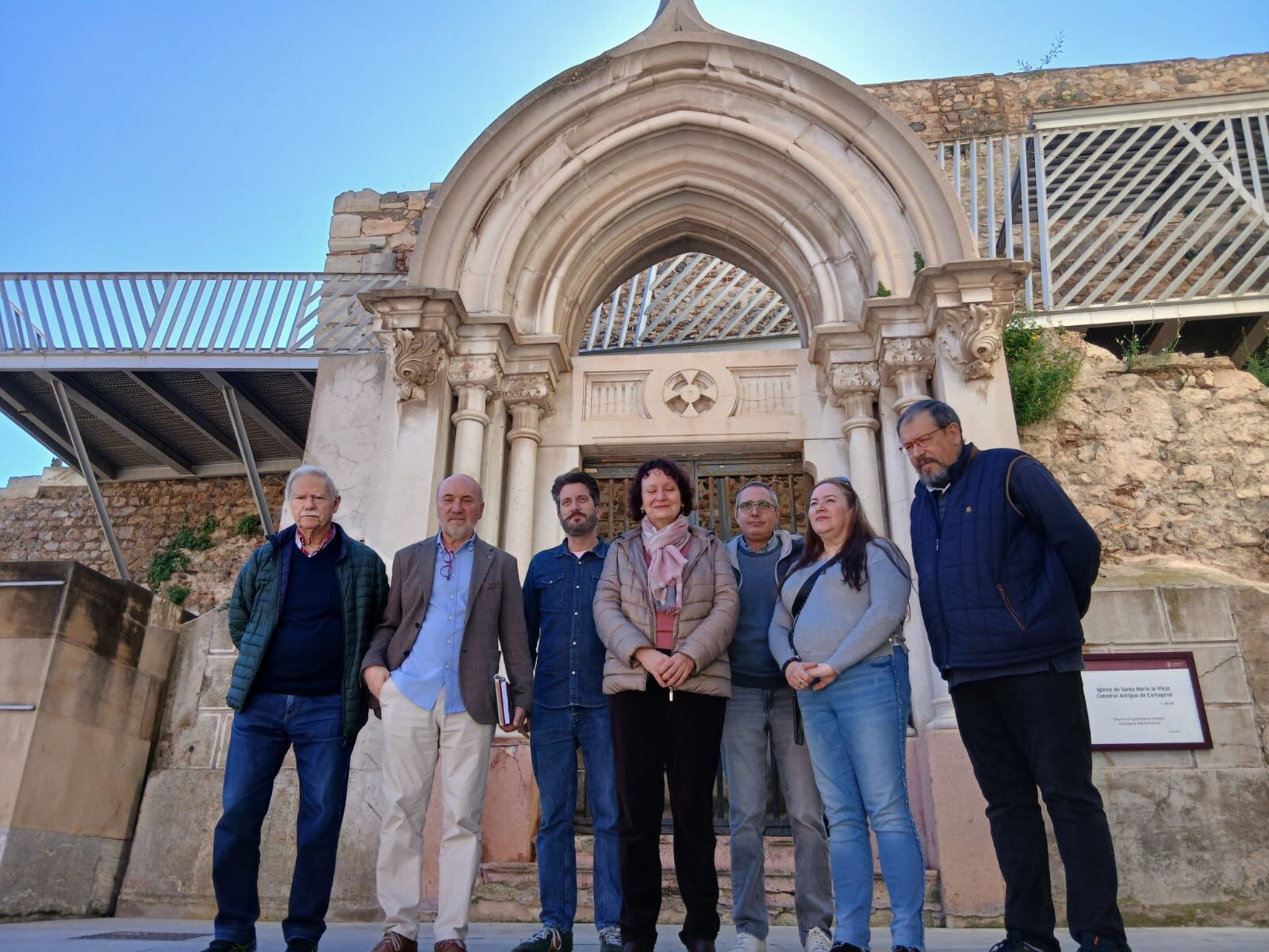 Miembros del GP Podemos-IU y de la Asociación Origen posan frente a las ruinas de la Catedral de Cartagena