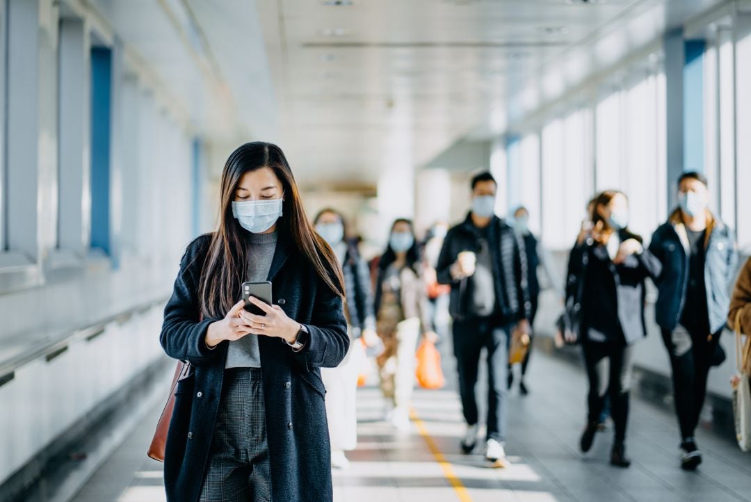 Una mujer utiliza su teléfono móvil con la mascarilla puesta.