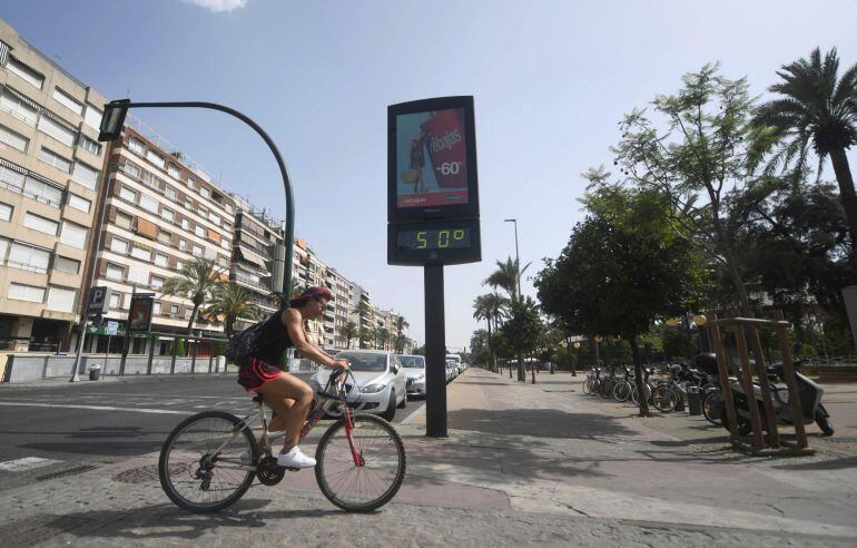 Un ciclista pasa junto a un termómetro que marca 50 grados en Córdoba, en una jornada marcada por la ola de calor que afecta a toda la Península.