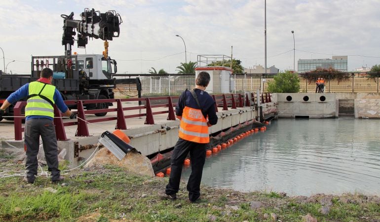 Operarios colocan la barrera anticontaminación en la desembocadura del Turia