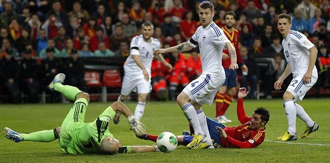 El delantero de la selección española David Villa, en el suelo junto al portero de Finlandia Niki Mäenpää ante los defensas finlandeses Joona Toivioy Jukka Raitala durante el partido de la fase de clasificación para la Copa Mundial de la FIFA Brasil 2014.