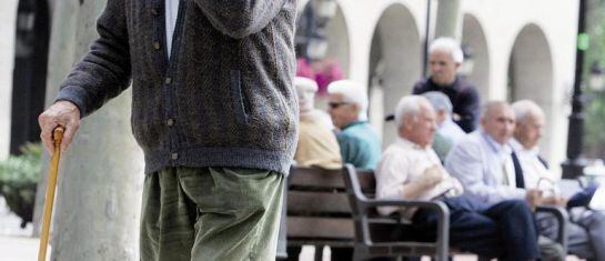 Un pensiona camina en primer plano mientras otros permanecen sentados en un banco