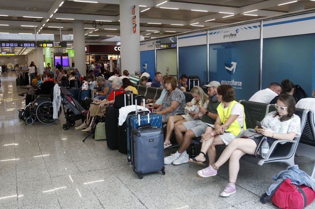 Varios turistas esperan sentados con sus maletas en el Aeropuerto de Palma (Baleares)