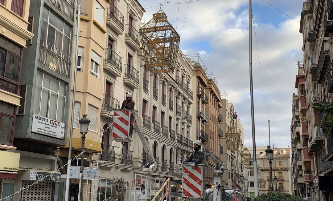 Dos operarios colocan las luces de Navidad en la calle Bernabé Soriano.