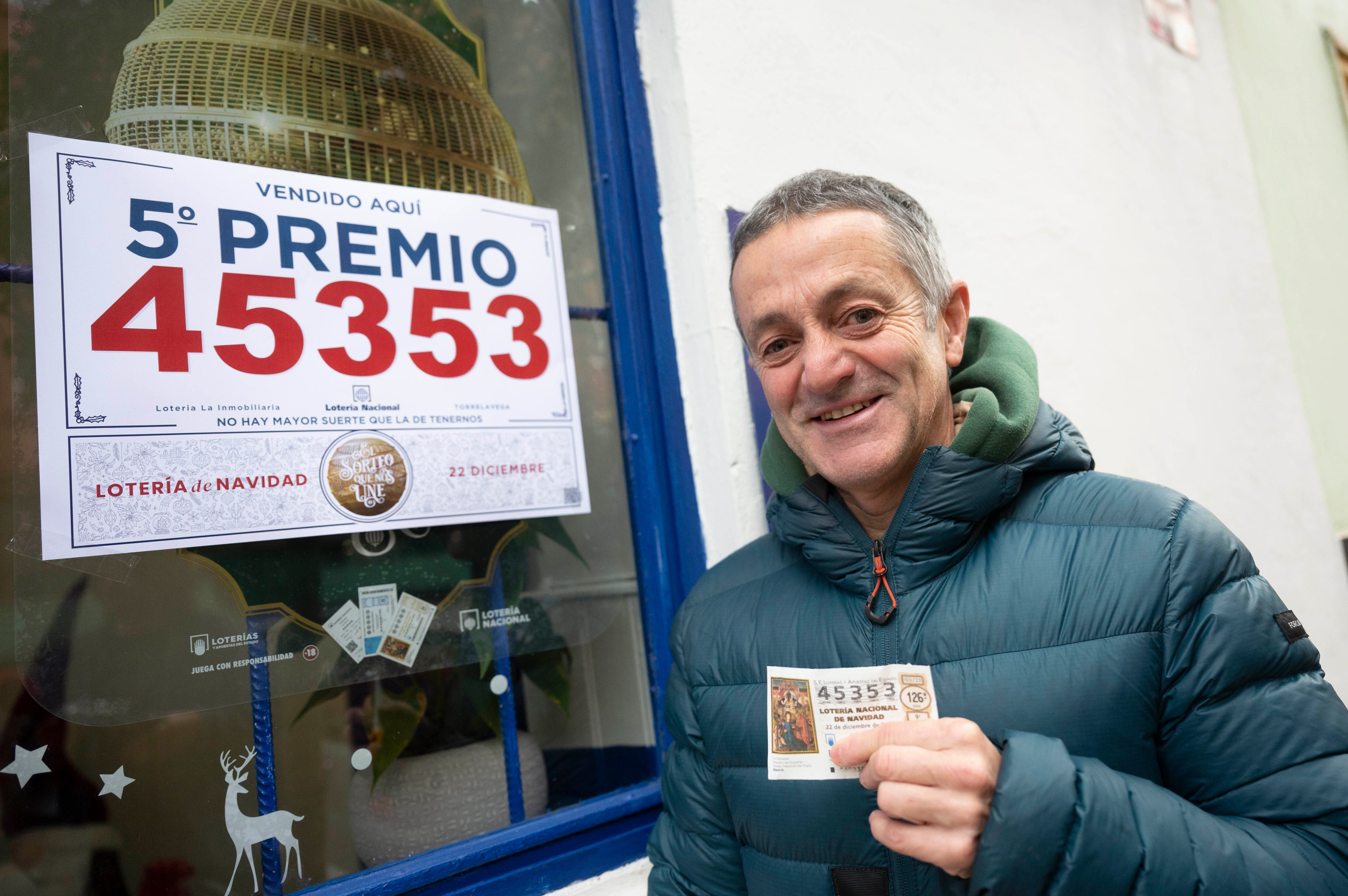 Un agraciado con un décimo del número 45.353, uno de los quintos premios del sorteo extraordinario de la Lotería de Navidad, posa ante la administración nº 6 de Torrelavega este viernes.