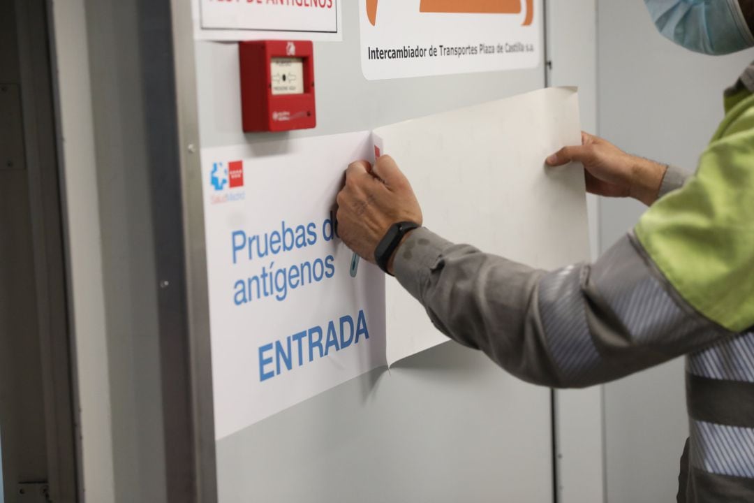 Un hombre pone un cartel que indica la entrada de realización de test de antígenos en un hospital madrileño.