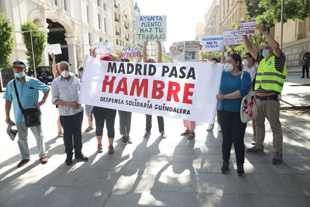 Varias personas sostienen una pancarta donde se puede leer &quot;Madrid pasa hambre&quot; ante el Palacio de Cibeles, sede del Ayuntamiento de Madrid