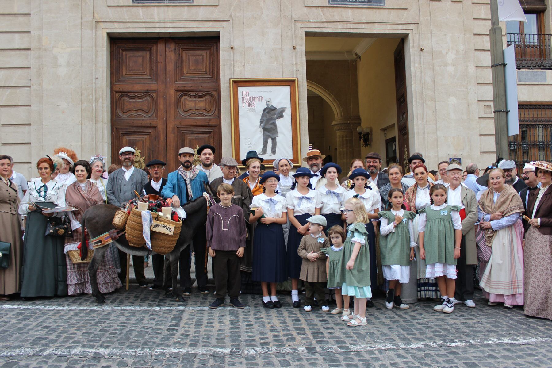 Los componentes del Grup de Danses Carrascal ante el cartel de la Feria Modernista