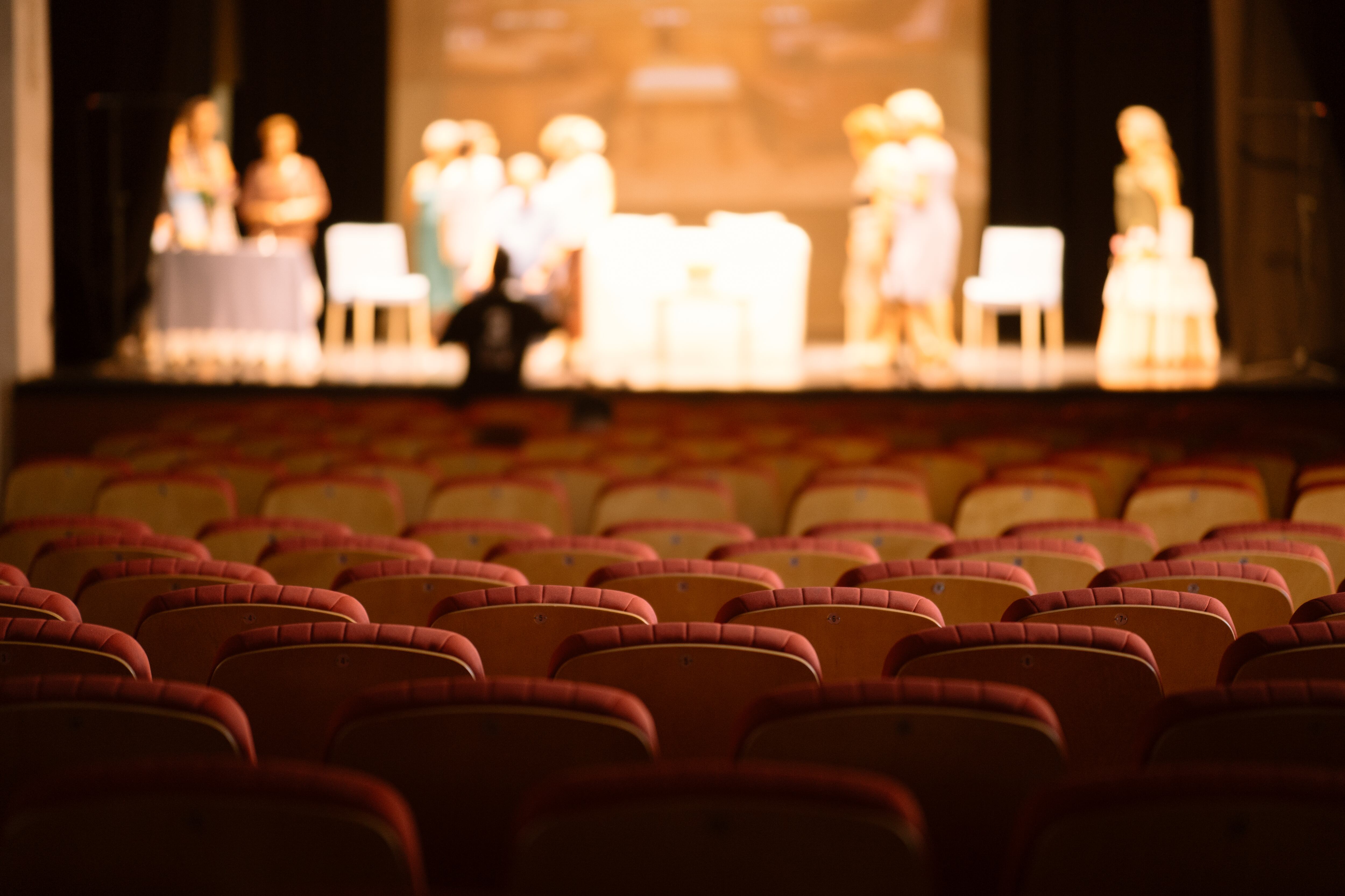 Empty theater red seats and a theater company  in a rehearsal session defocused at background