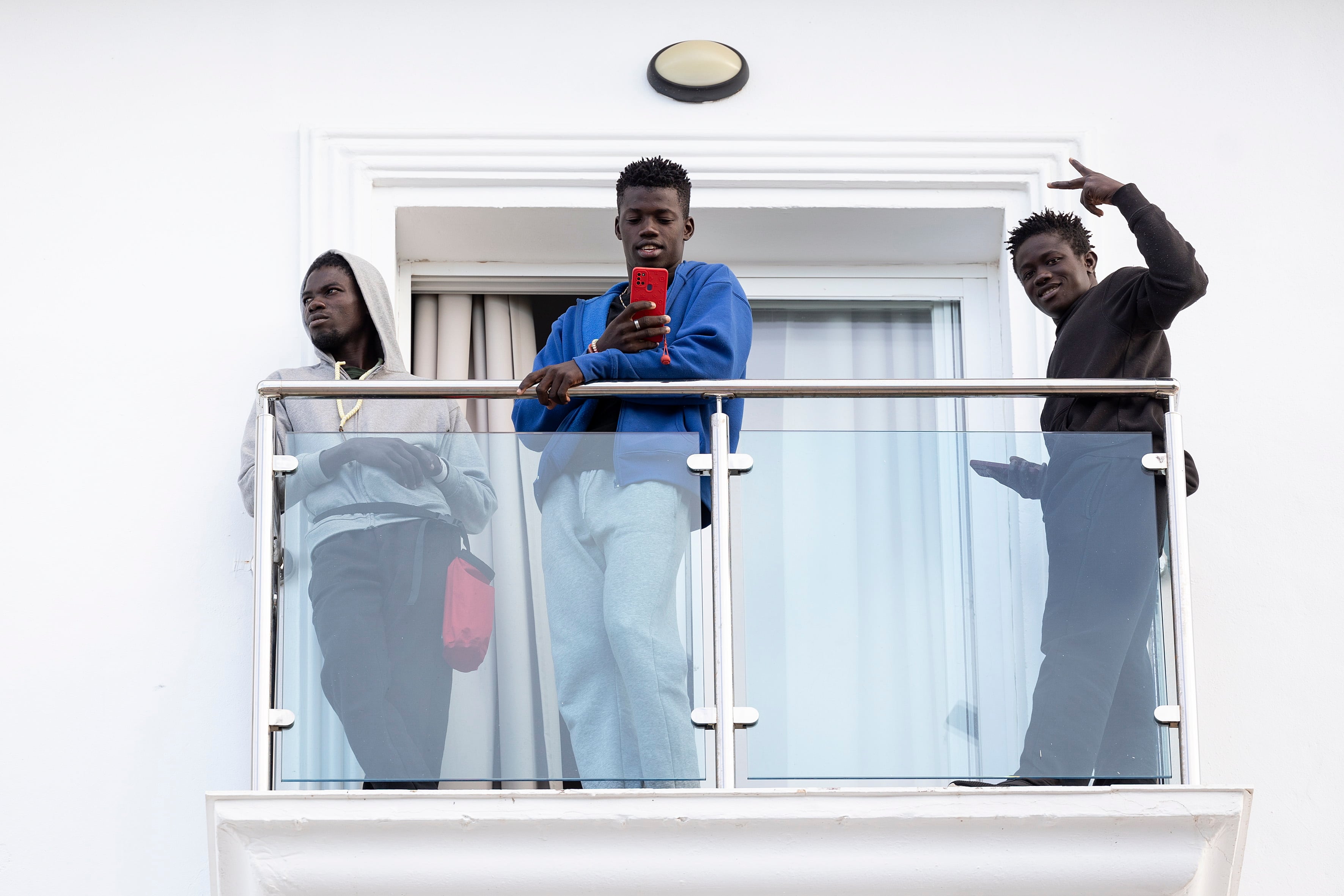 GRAFAND5936. TORROX (MÁLAGA), 25/10/2023.- Algunos de los 240 inmigrantes de origen subsahariano llegados en los últimos días a Canarias saludan desde la terraza de una habitación del hotel Urban Beach de la localidad malagueña de Torrox donde se alojarán tras ser trasladados por el Gobierno, con la colaboración de la Cruz Roja. EFE/Daniel Pérez
