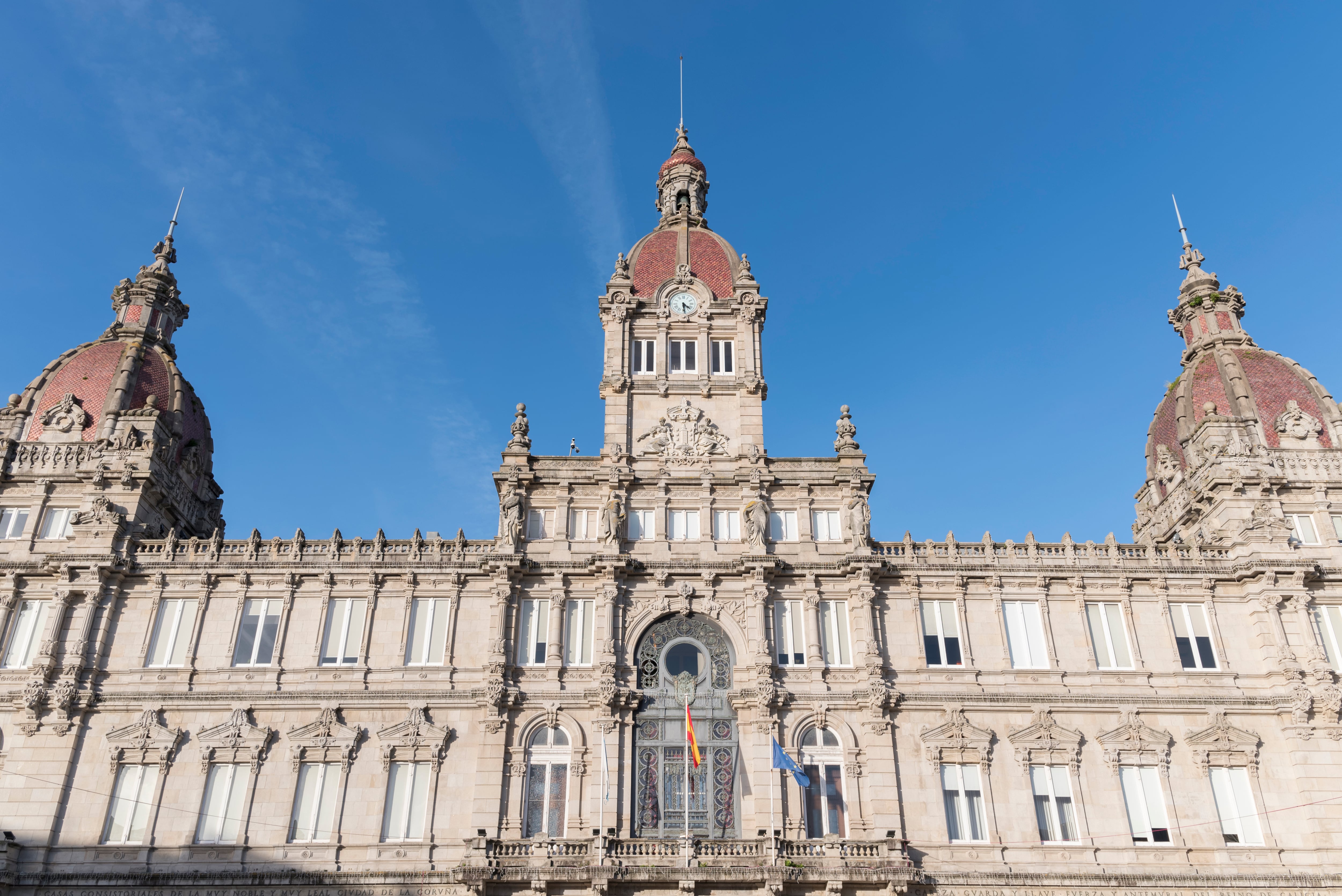 The grand facade of the City Hall of A Coruña, Spain, showcasing its neo-baroque architecture with intricate details and iconic domes under a clear blue sky. Perfect for travel guides, cultural materials, or architectural references.