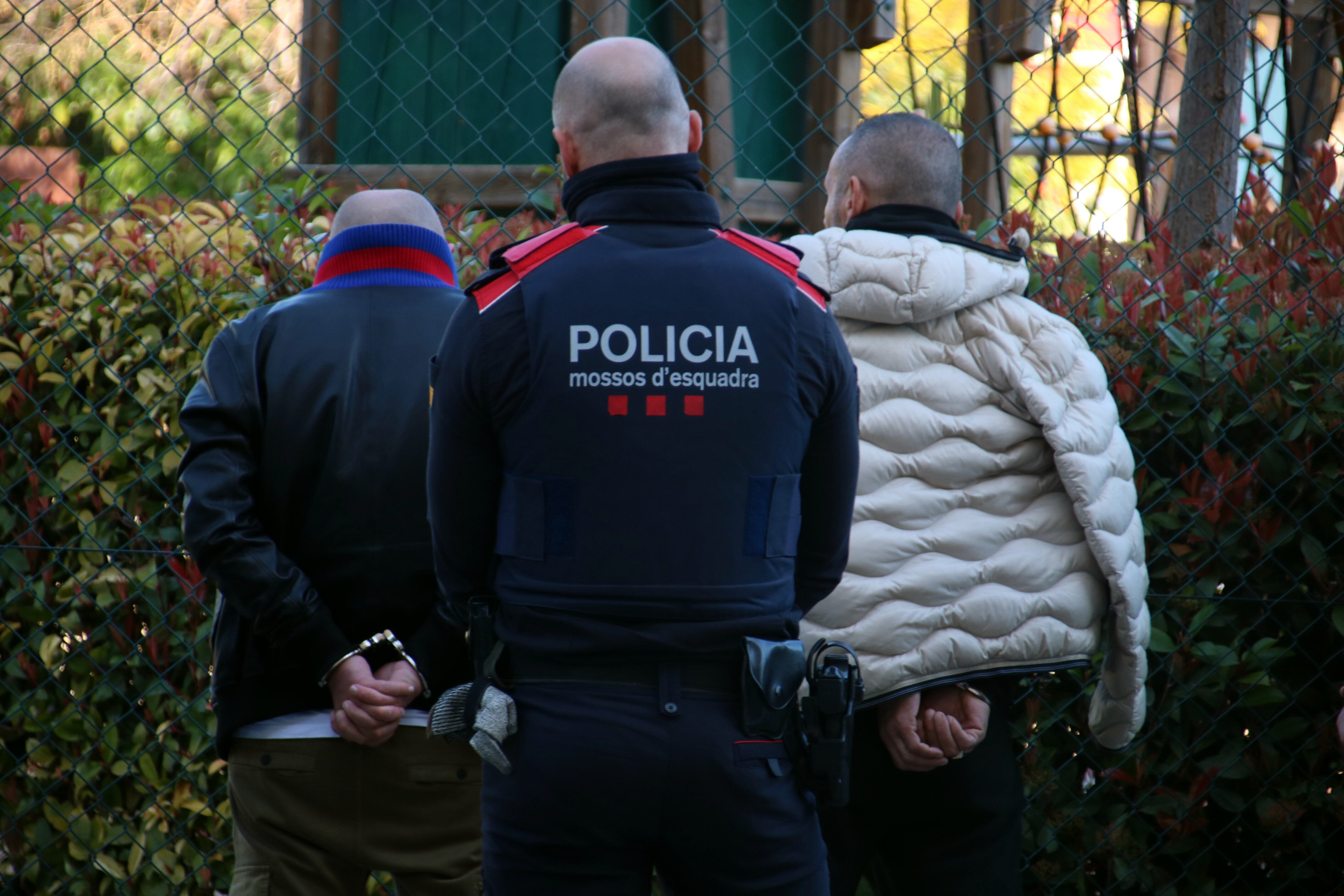 Un agent dels Mossos d&#039;Esquadra custodiant dos detinguts en l&#039;escorcoll fet a dos vehicles en el marc de l&#039;operatiu policial contra un grup investigat per tràfic de drogues i falsificació de moneda