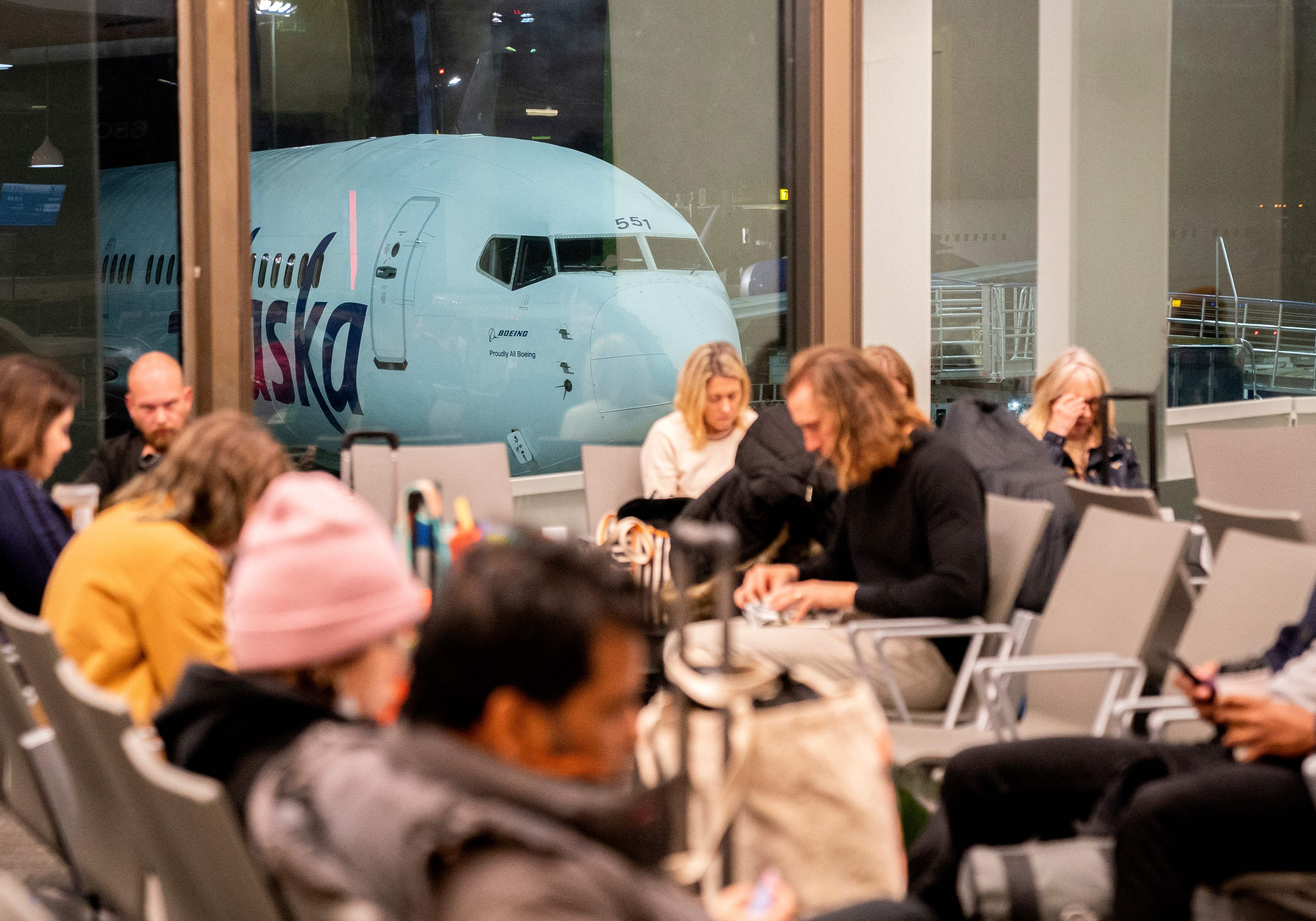 Los viajeros esperan en la terminal del Aeropuerto Internacional de Los Ángeles mientras un avión de Alaska Airlines está parado frente a una puerta de embarque