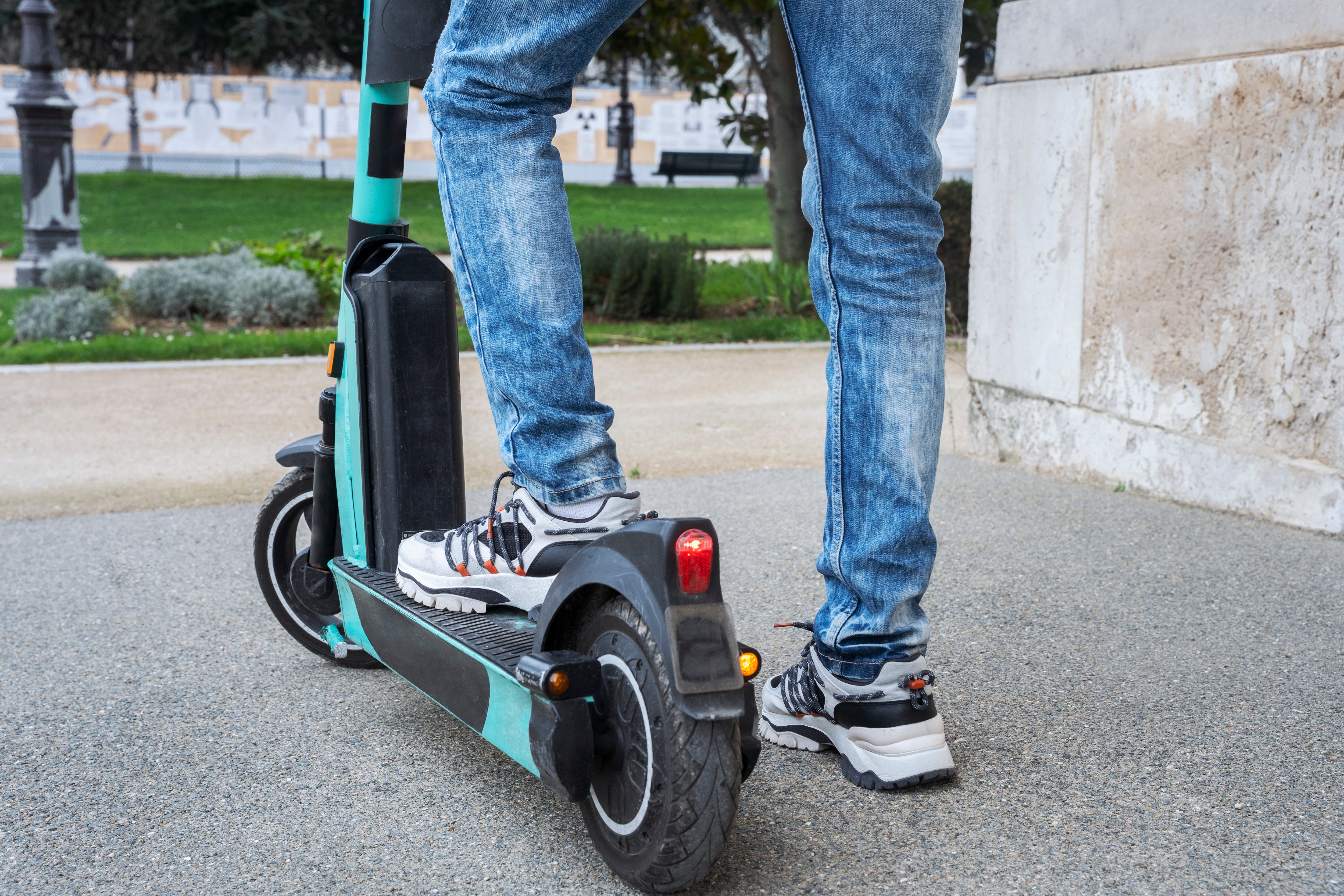 Un joven con su patinete junto a un parque