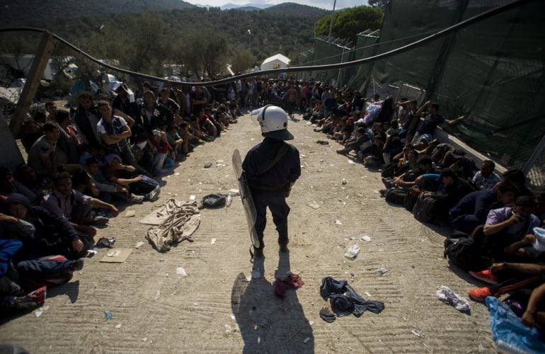 Un policía griego mantiene el orden mientras un grupo de inmigrantes esperan para ser registrados en un campamento para refugiados.