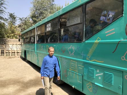 Un niño pasea por delante del autobús-biblioteca verde