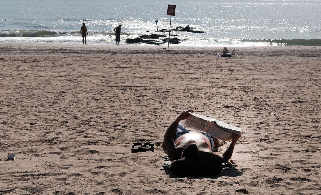 Un lector aprovecha la tranquilidad de una playa para leer un periódico.