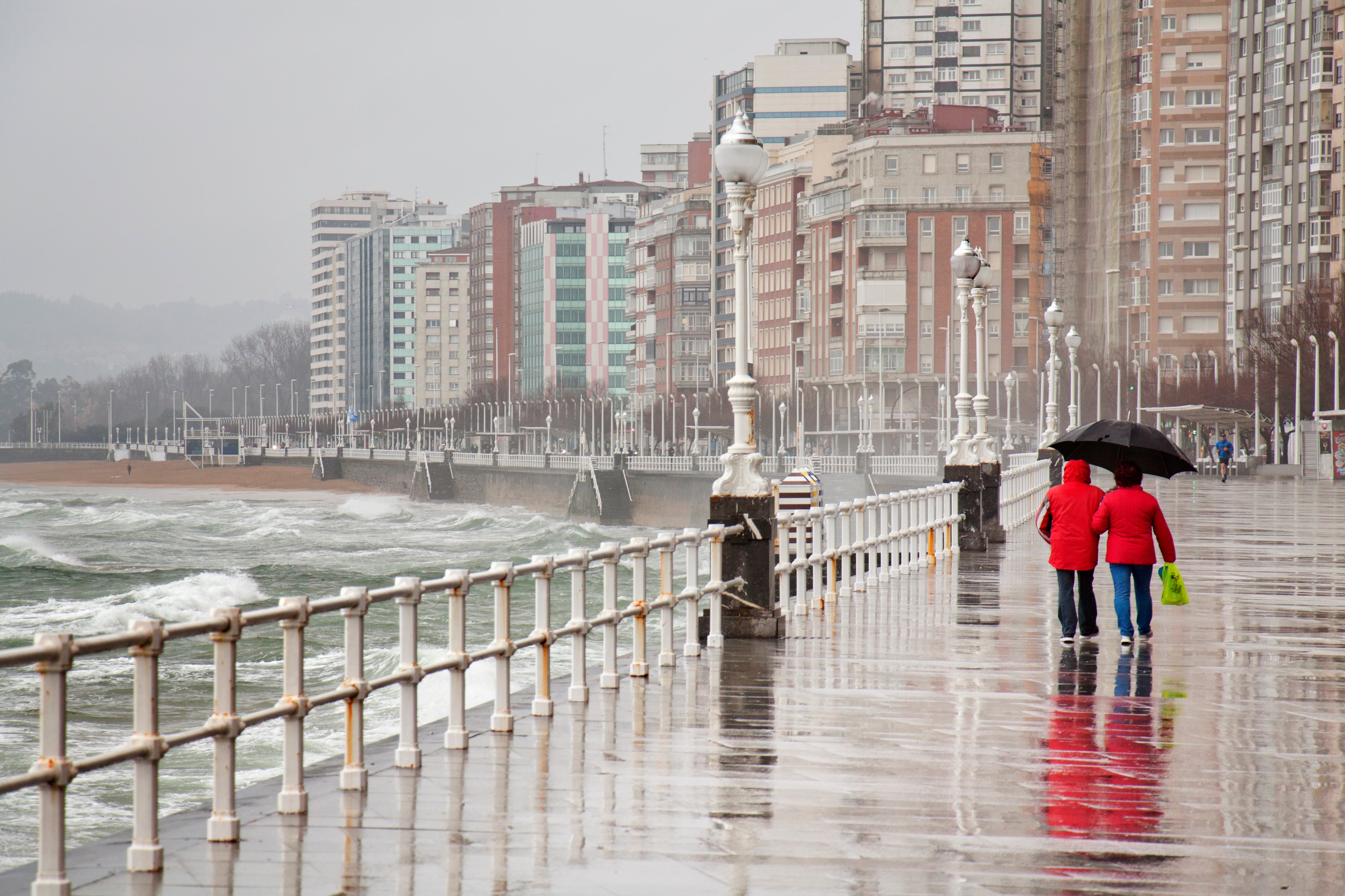 A woman with an umbrella looking at the sea in a rainy day in San Lorenzo Beach in the city of Gijon, Asturias (Spain).