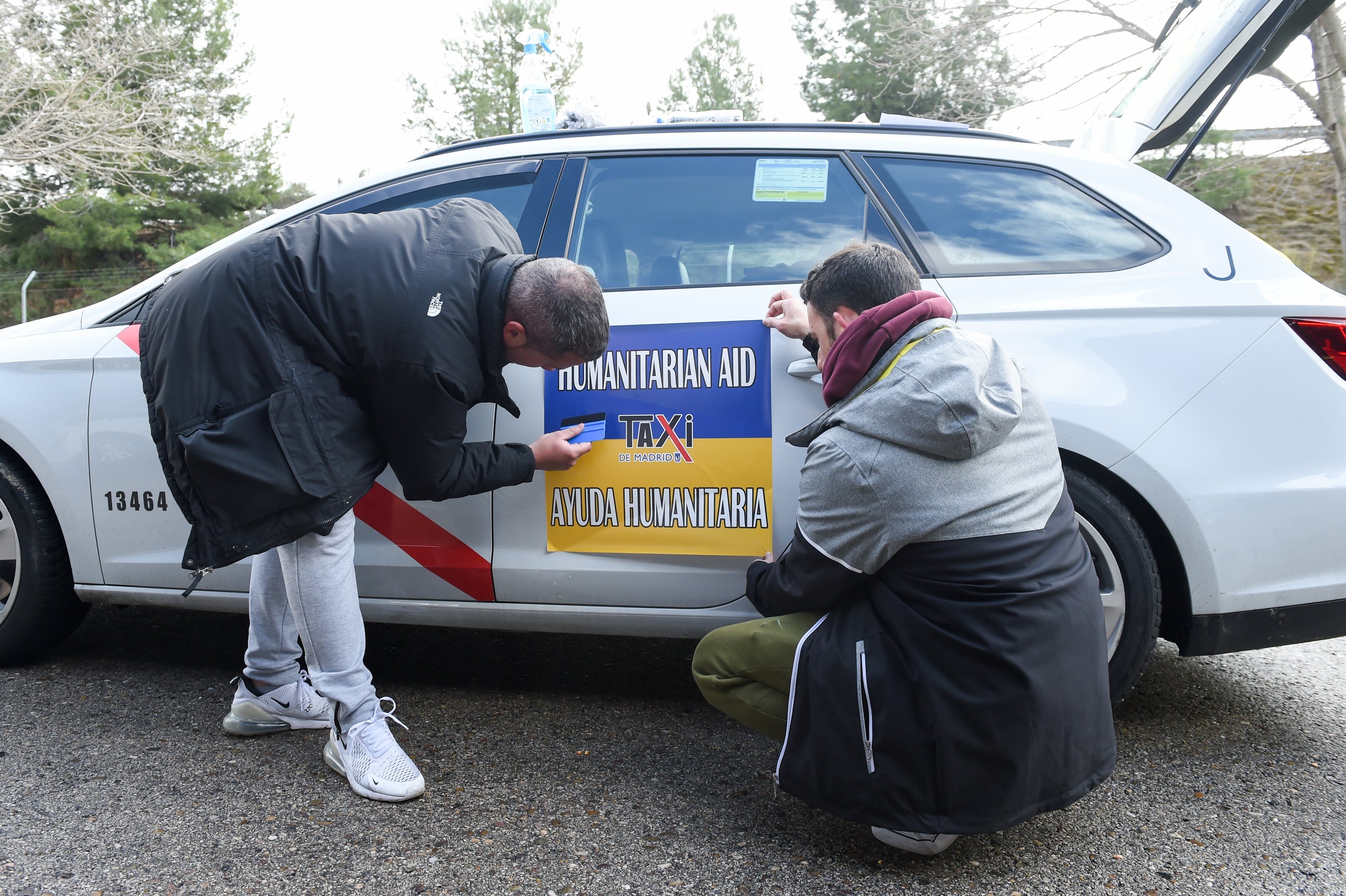 Dos taxistas colocan una pegatina identificativa de la caravana humanitaria que se dirige a Polonia para trasladar refugiados ucranianos.