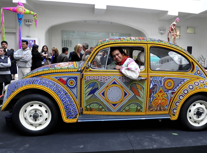 Un indígena huichol posa en Ciudad de México, junto a un automóvil Volskwagen escarabajo