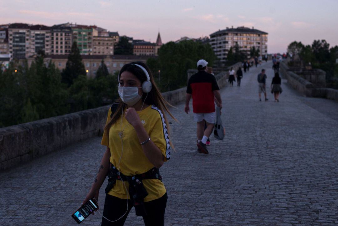 Una joven con mascarilla camina por el puente romano durante las horas permitidas