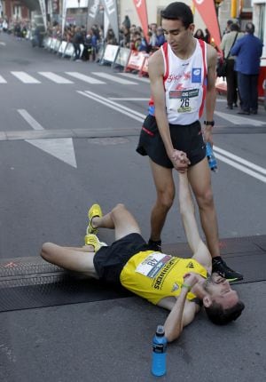 GRA096. GIJÓN, 31/12/2015.- El corredor Marcos Peón es ayudado por el segundo clasificado el joven Jossuef Benkert (de pie) tras llegar a la meta y conseguir su undécima victoria en la 46 edición de la San Silvestre de Gijón, la más veterana y más numerosa en participantes de las 31 que se disputan en Asturias en este último día del año y que está organizada por el club Gijón Atletismo. EFE/Alberto Morante